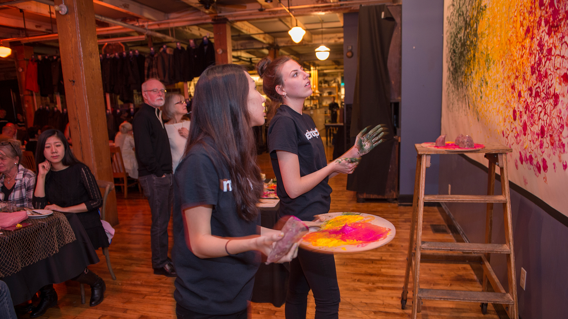 Two students looking up at mural holding paint items
