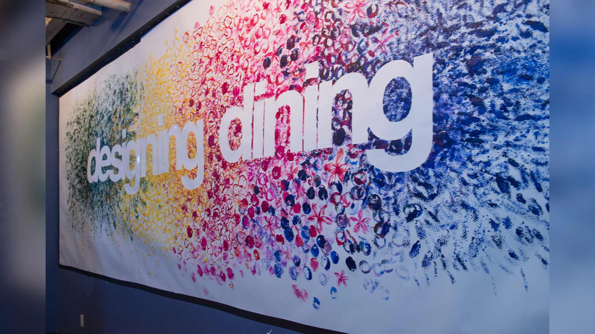 Angled view of stamped mural with green, yellow, red, and blue paint with logo in white in center