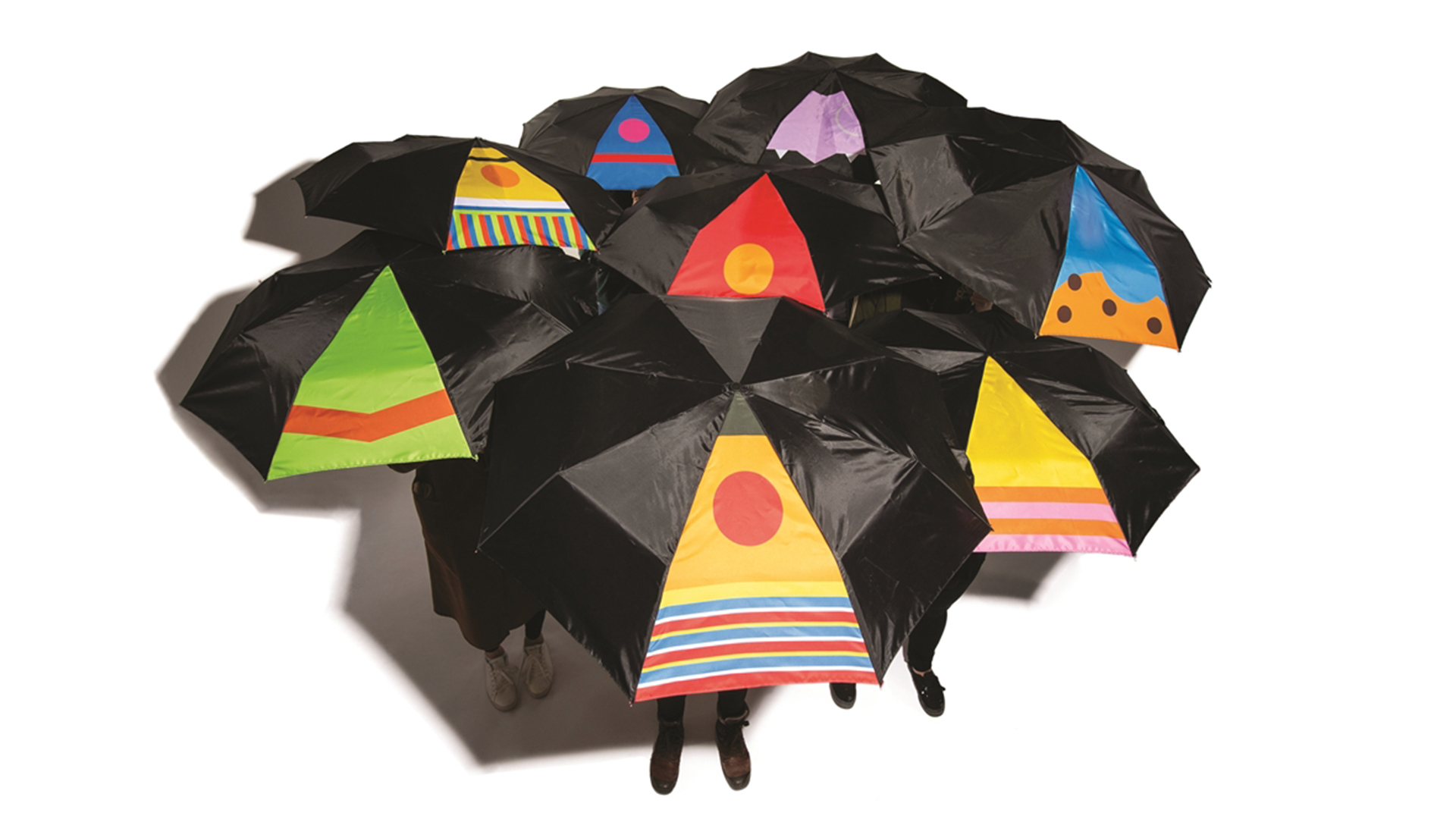 8 umbrellas open with people obscured underneath, each mostly black with one section of bright color