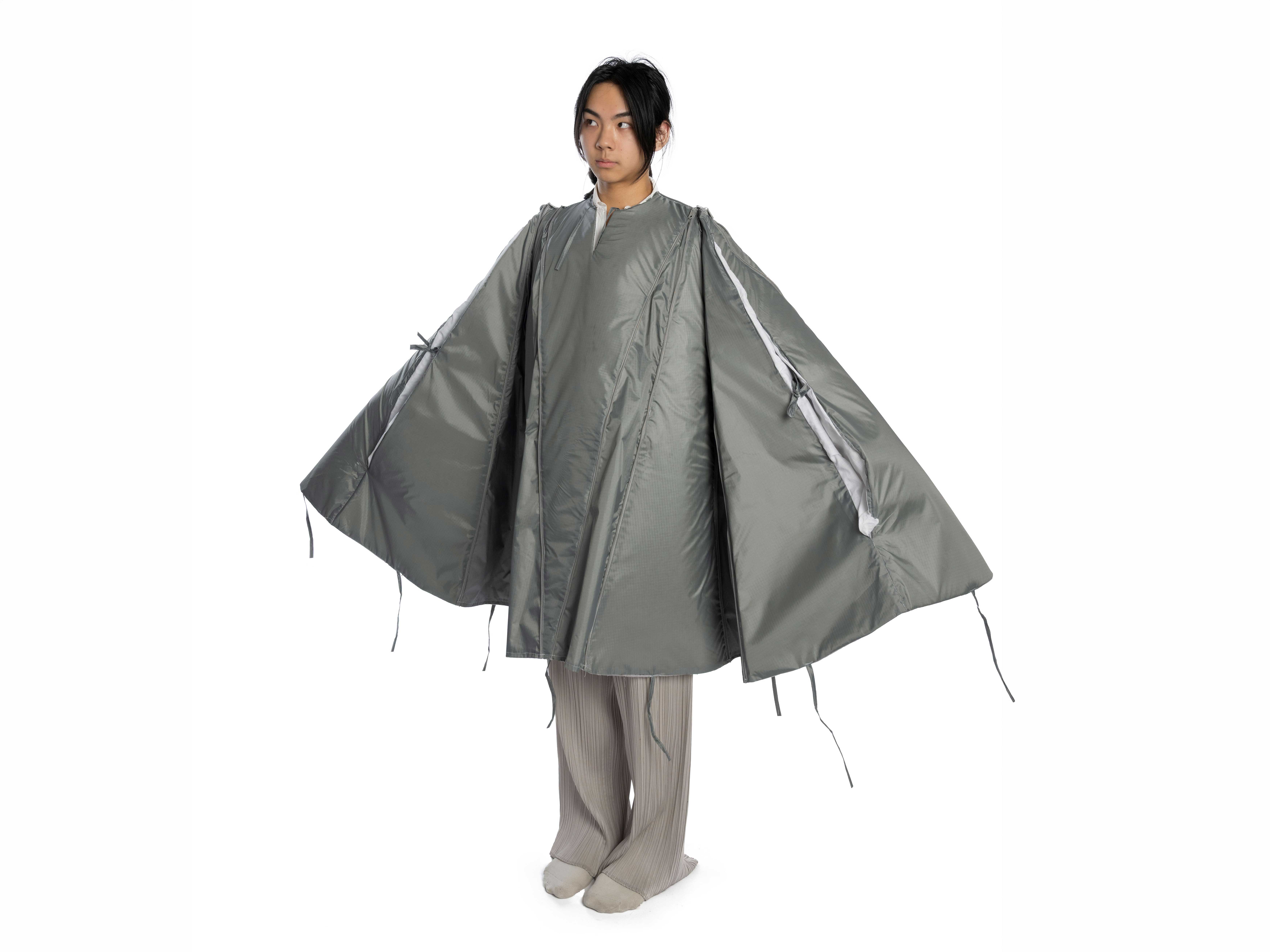 Photo of a women standing wearing the Cloak model with her arms slight open to show the cloak's shape. 
