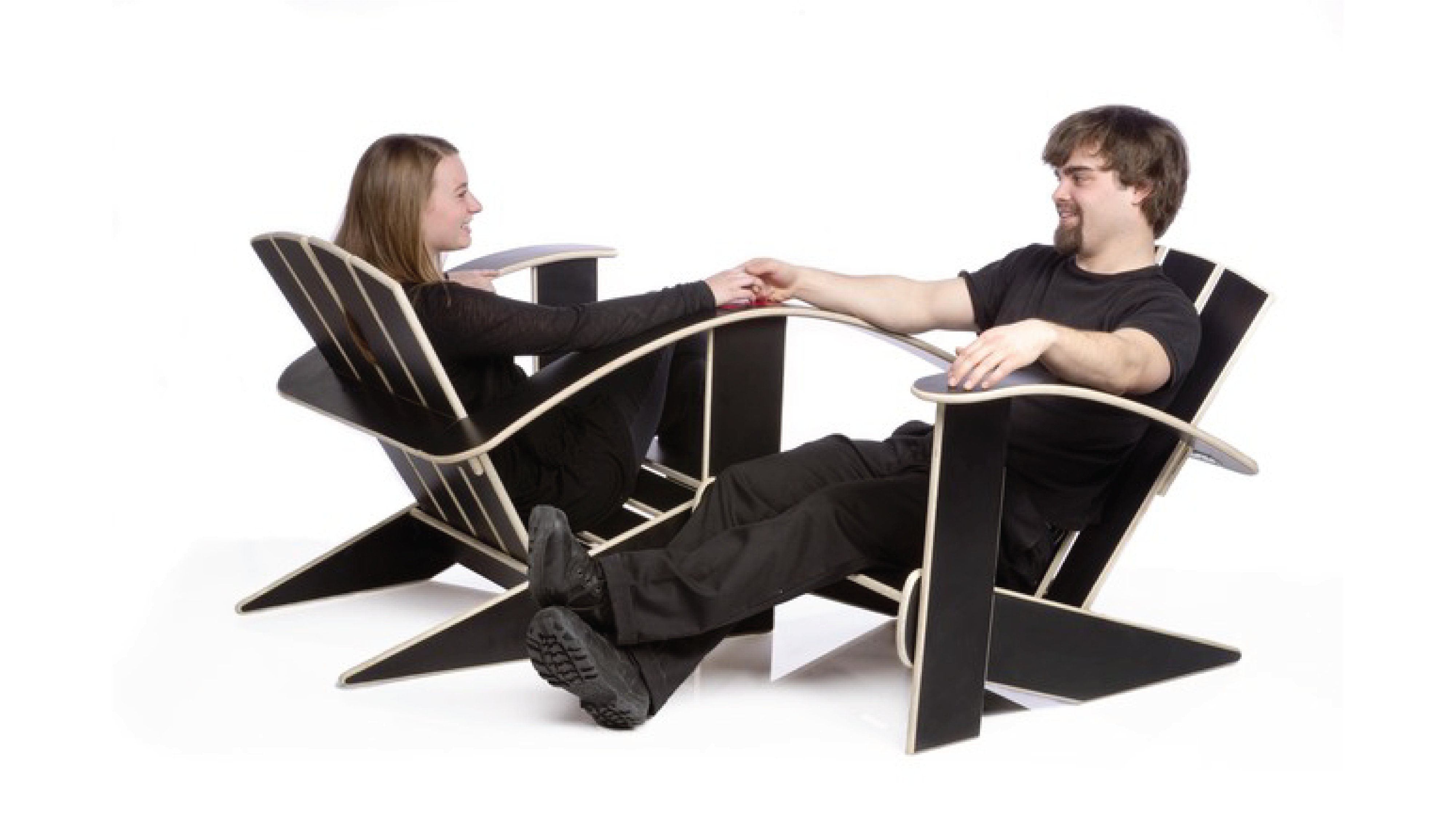 People holding hands at a two Adirondack-style chairs oriented towards each other that share a common armrest.