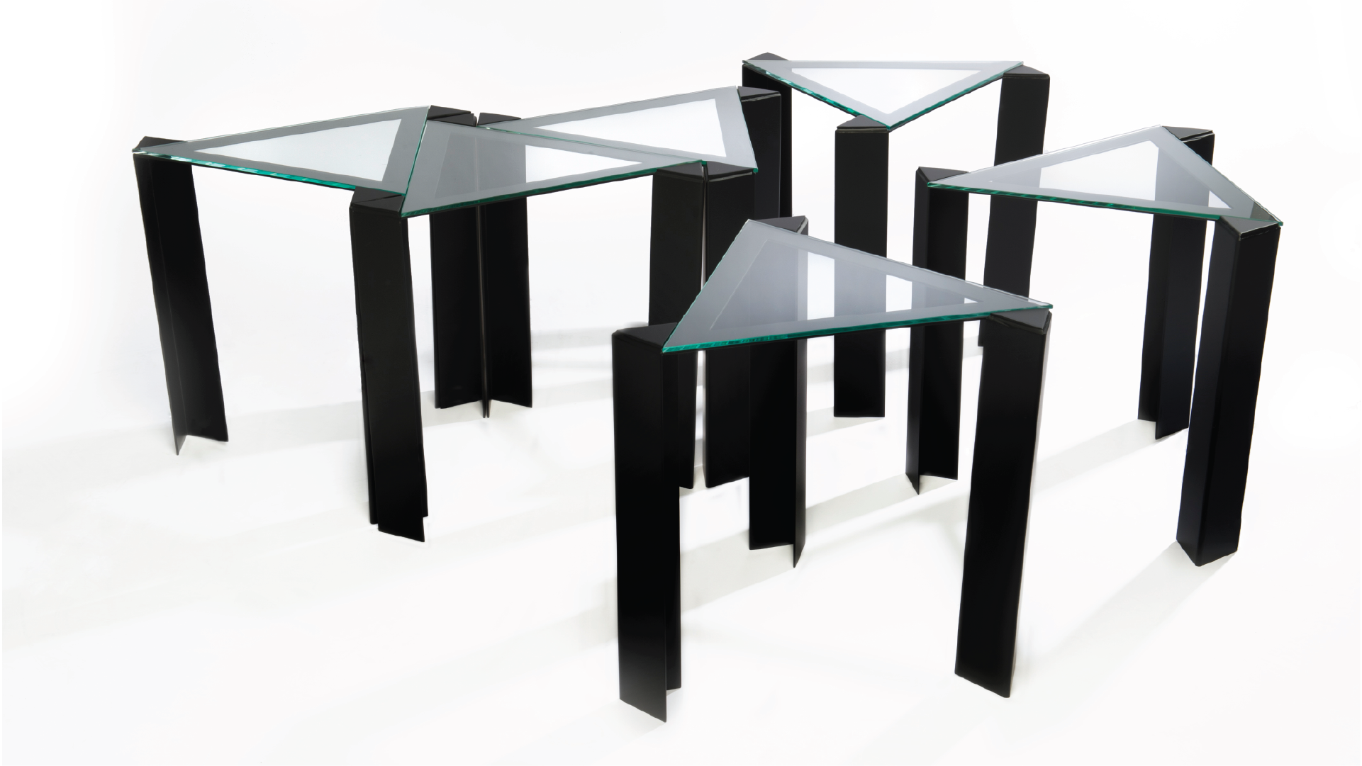 A series of six stainless steel tables in a triangular shape with glass tabletops. The tables are all spread out.