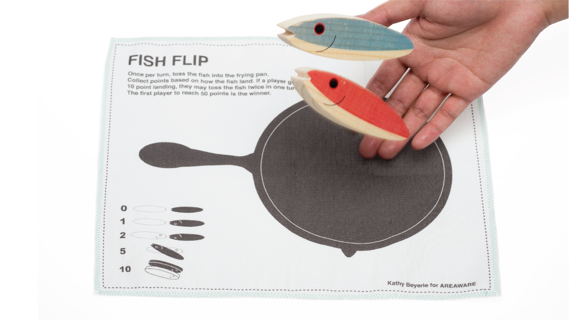 Hand placing 2 wooden toys in a fish shape on the top of the cloth play set.