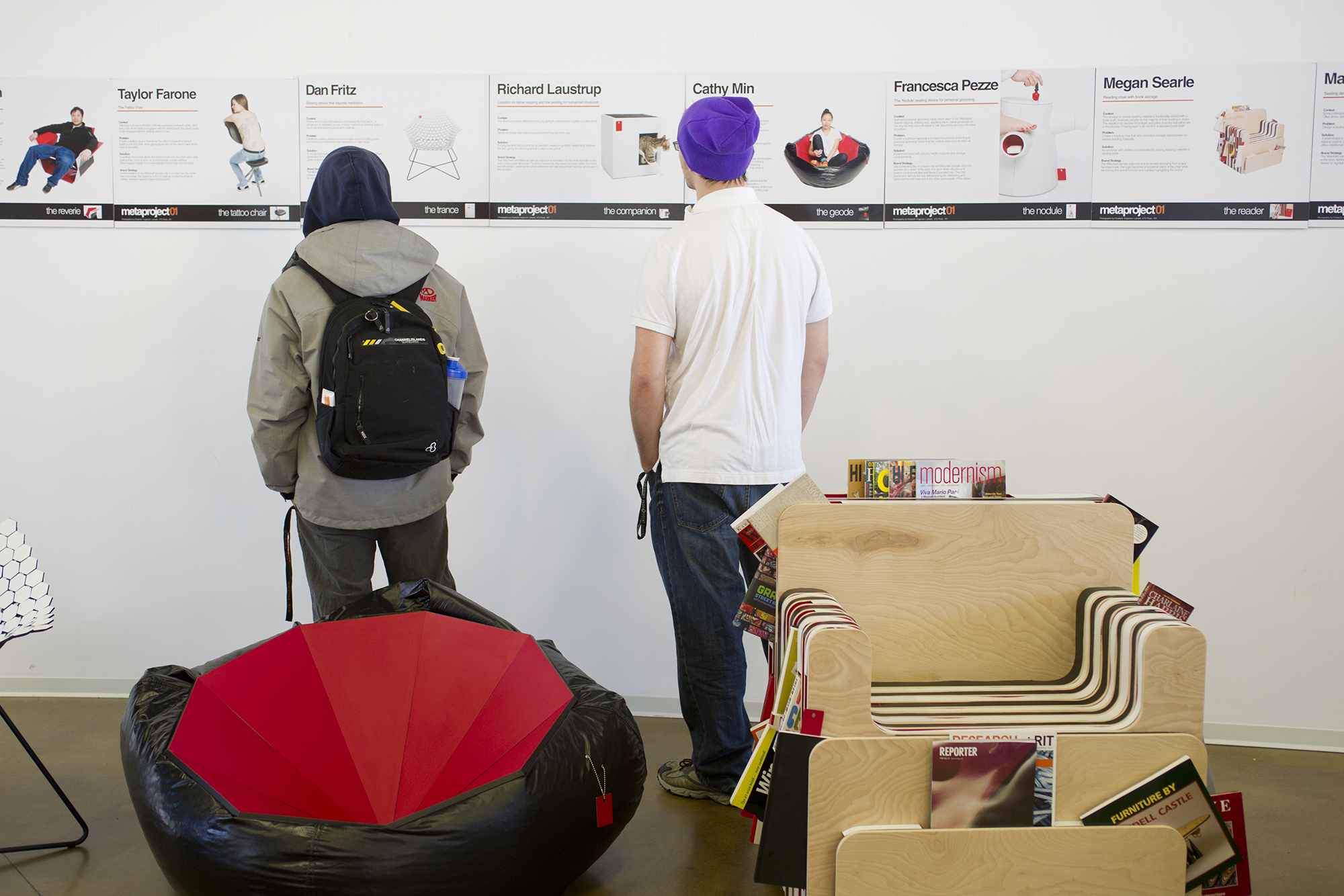 Two people view posters of designs on a wall.