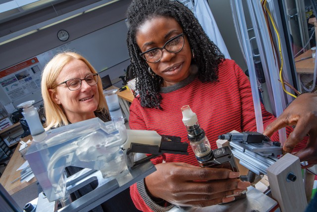 researcher watches as college student adjusts a vape pen on lab equipment.