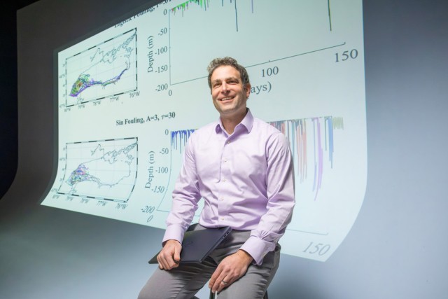 a man in a purple shirt sits in front of a screen showing data