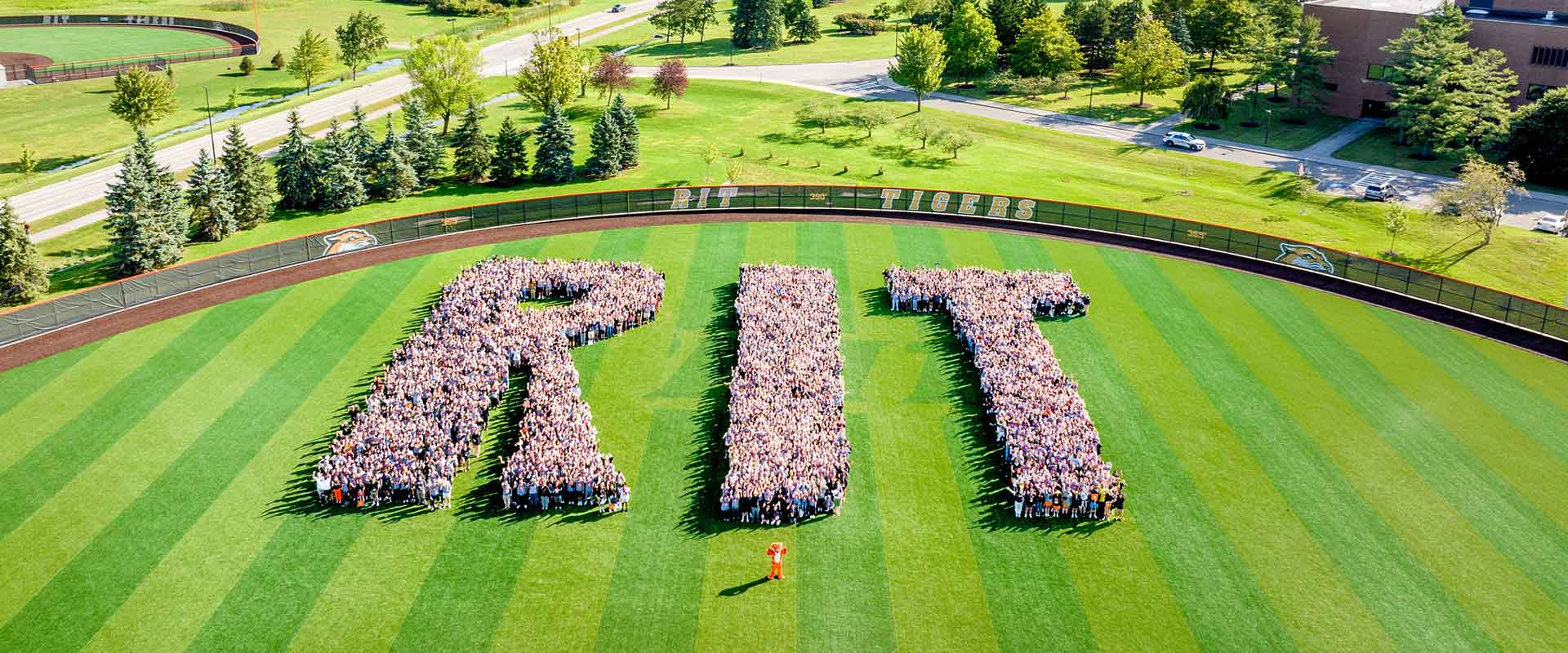 aerial view of the outfield of a baseball field, with hundreds of students gathered to form the shape of the letters R I T.