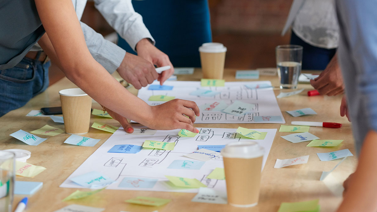 closeup of people collaborating on a project on a table with sticky notes.