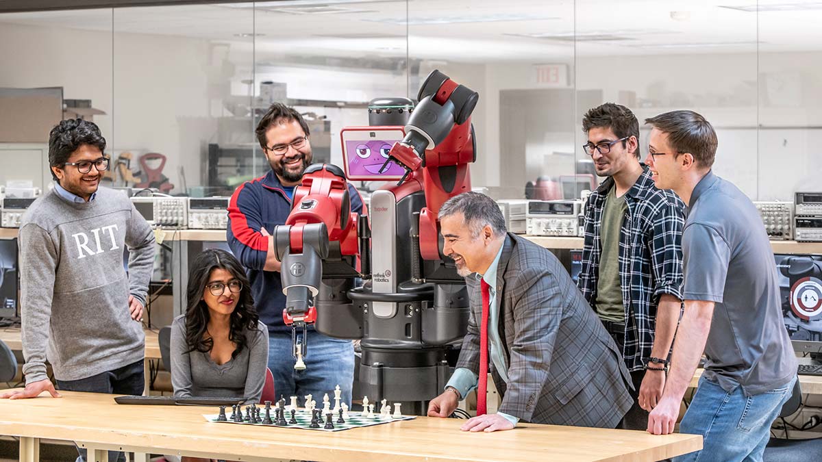 a group of students and a professor watch a robot play chess.