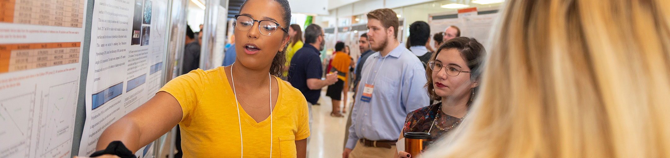 a student points to a poster presentation during a research symposium.