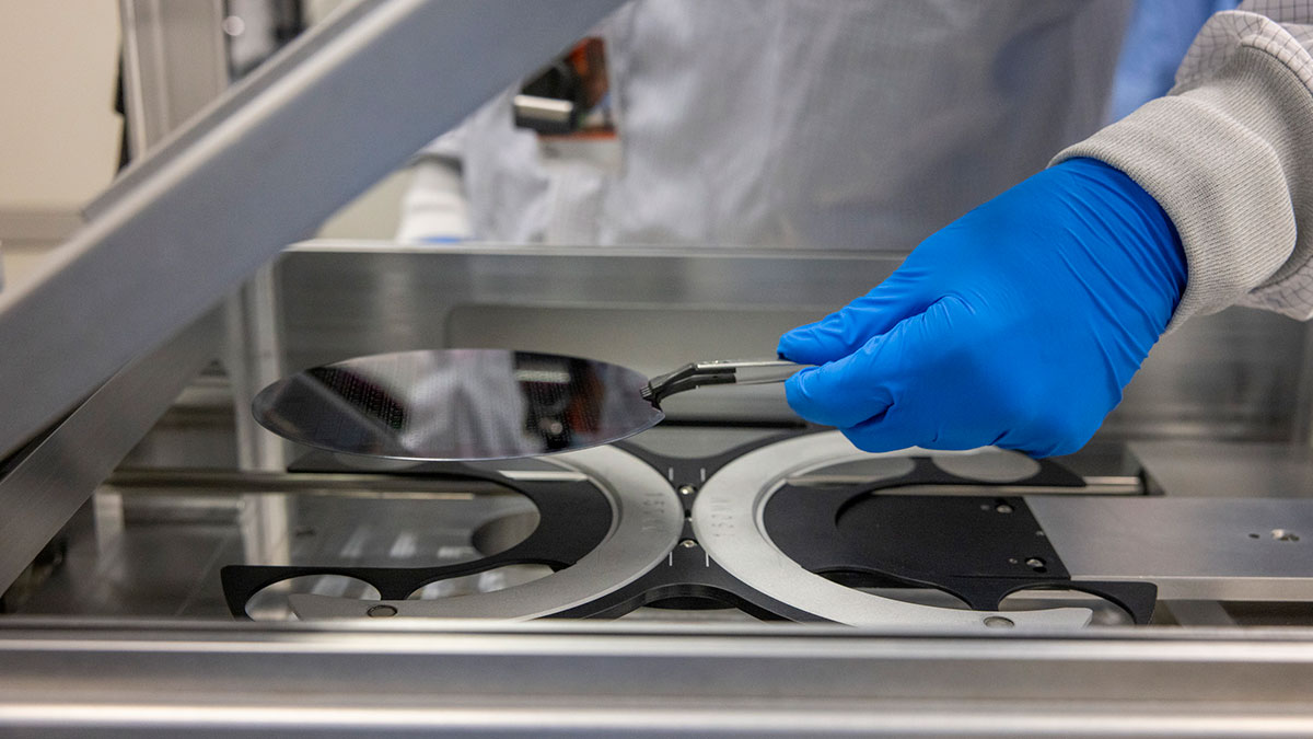 closeup of a person's gloved hands carefully placing a round semiconductor wafer into a machine.