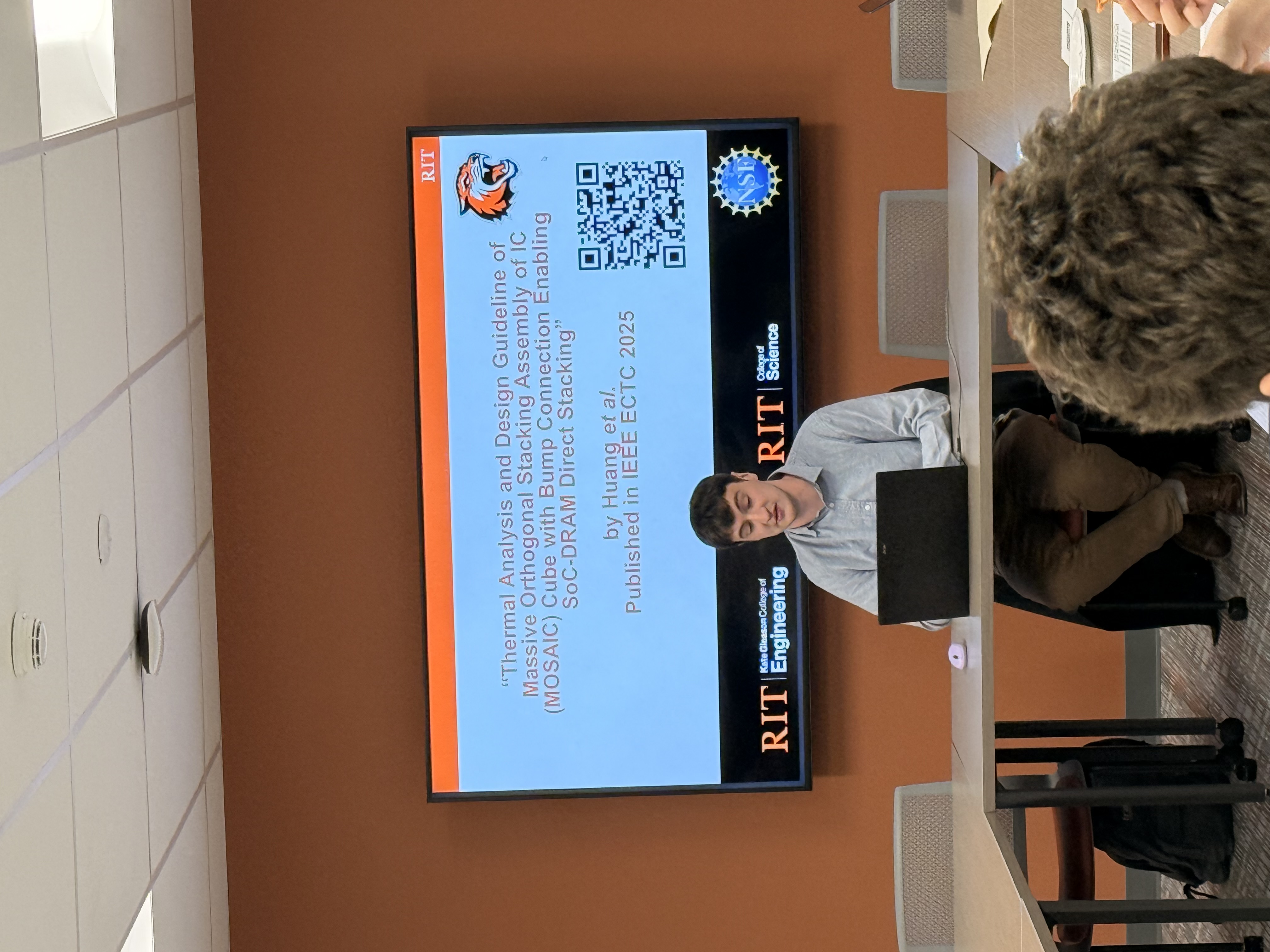 Image of a male student sitting in front of a projection screen presenting to a group of students
