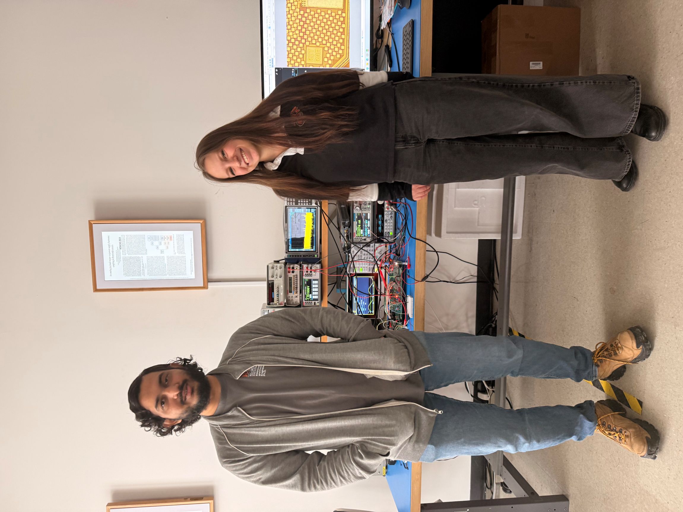 A male and female student smiling in front of lab equipment