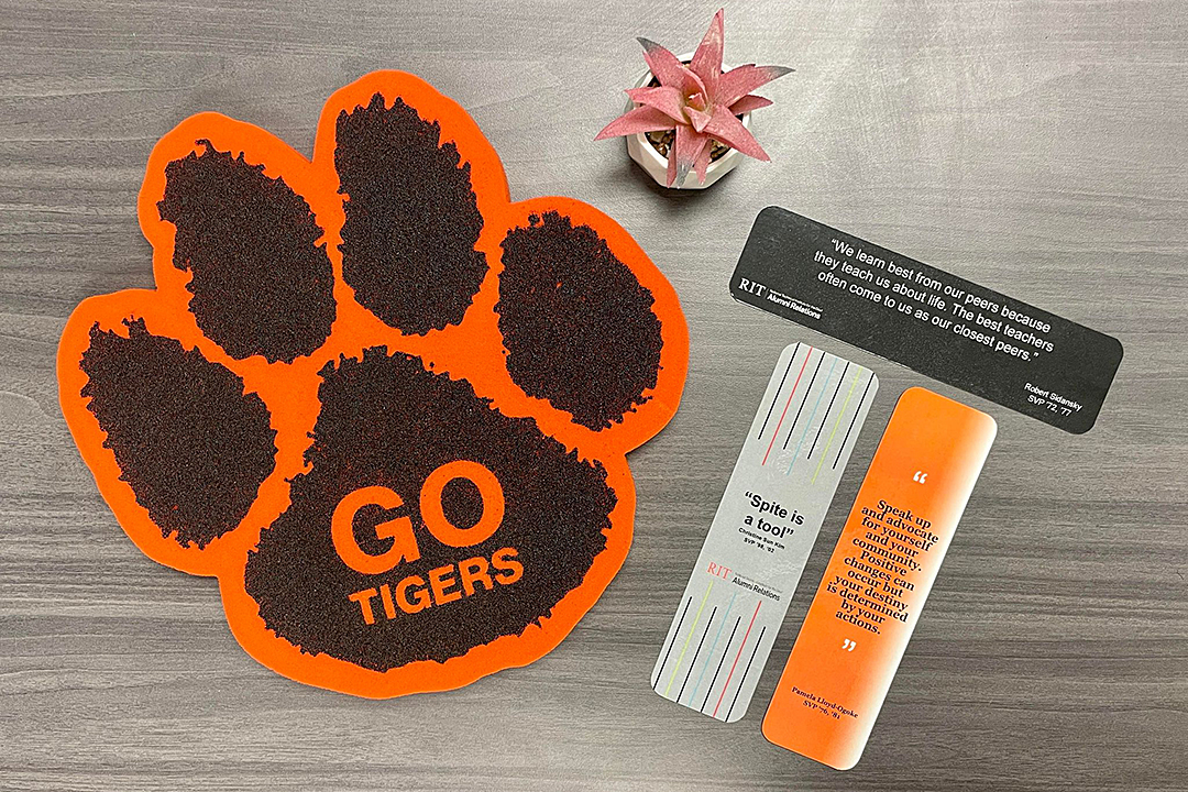 Photo of large orange tiger paw with text 'Go Tigers', small potted pink succulent, and the back side of three bookmarks.