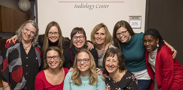 Photo of audiologists in front of sign that says Communication Studies and Services Audiology Center; shows 6 women in back row standing and 3 women in front sitting.