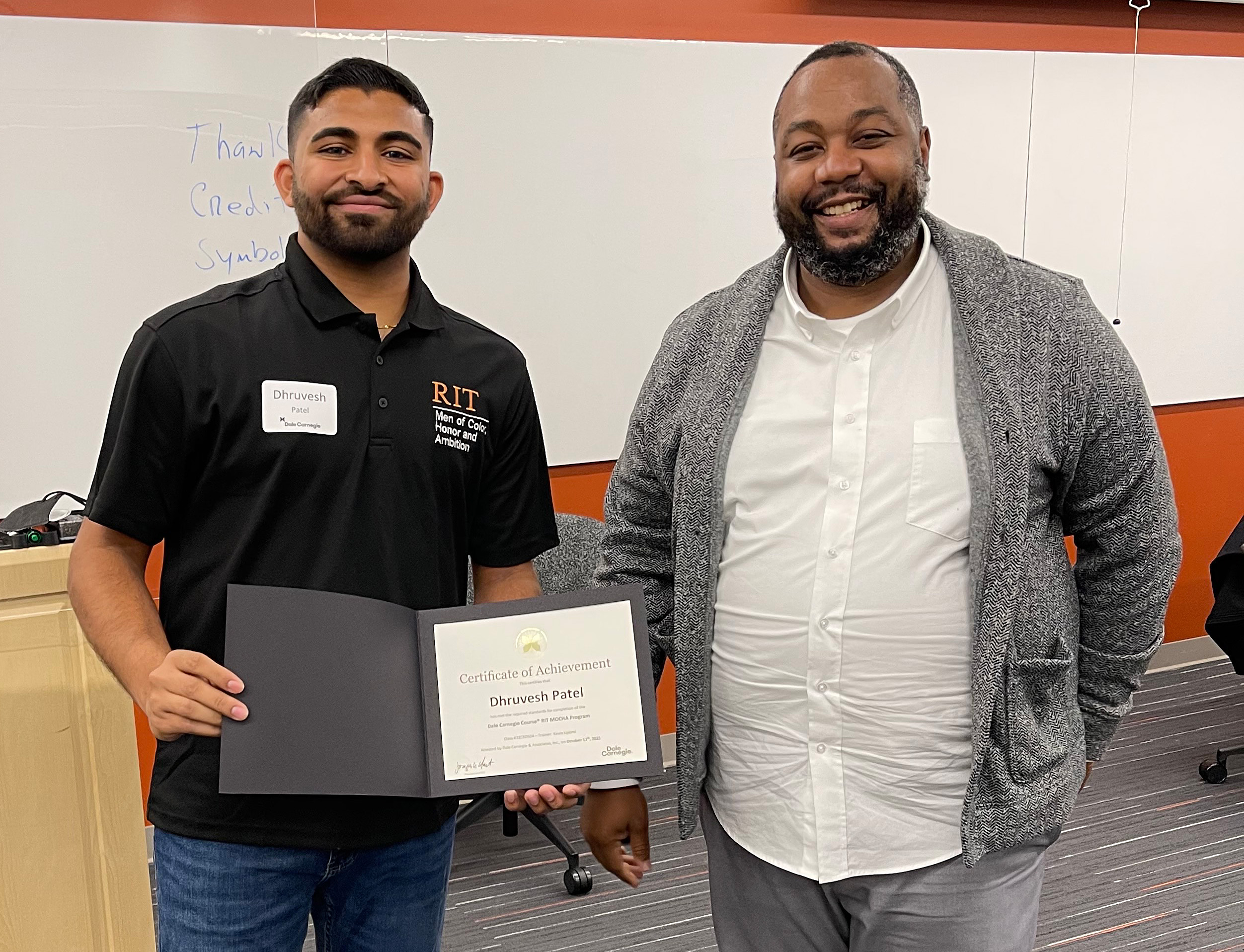 Photo of Dhruvesh holding a certificate of achievement from the Dale Carnegie course, standing next to a man