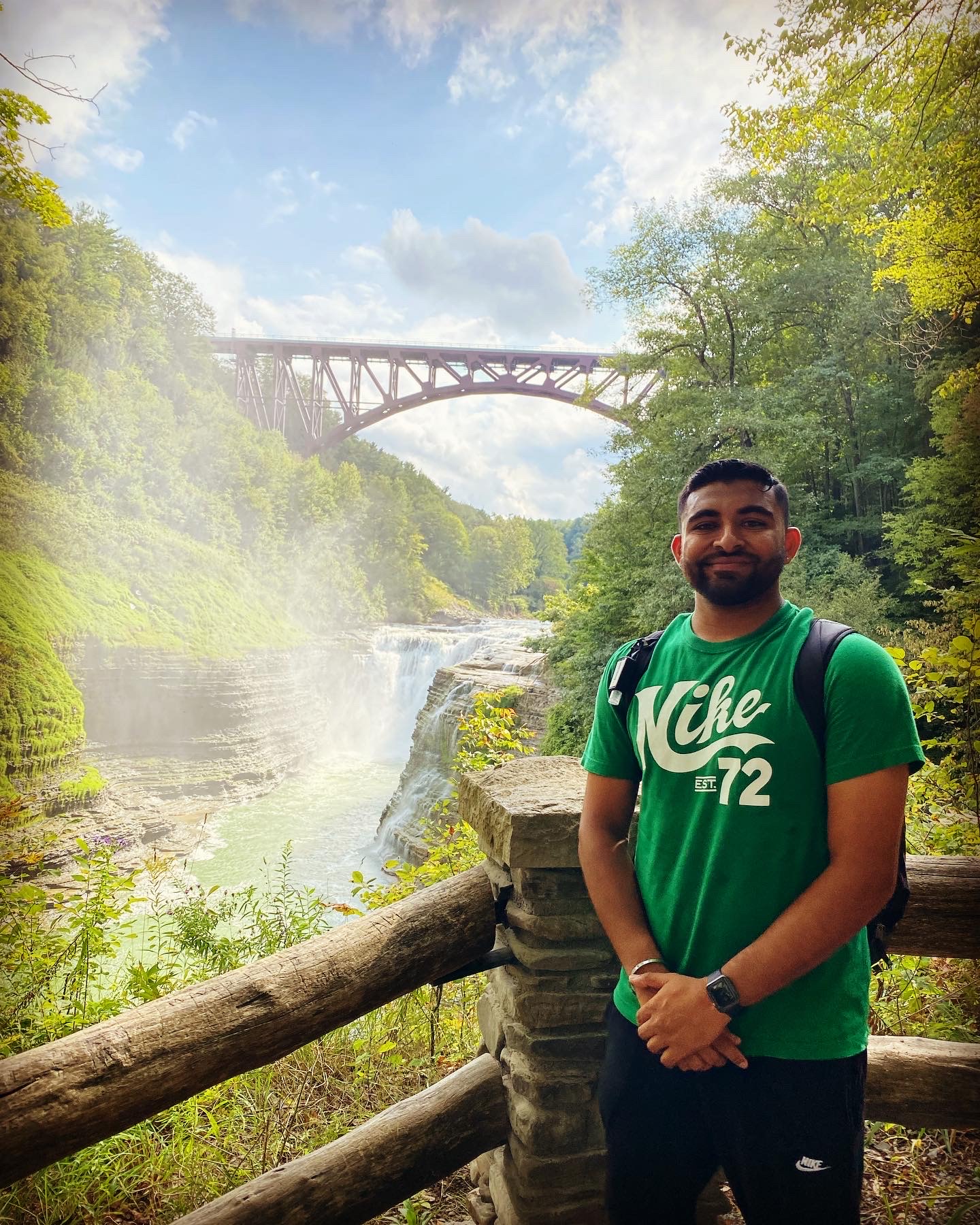 Photo of Dhruvesh standing in front of a waterfall and trestle bridge