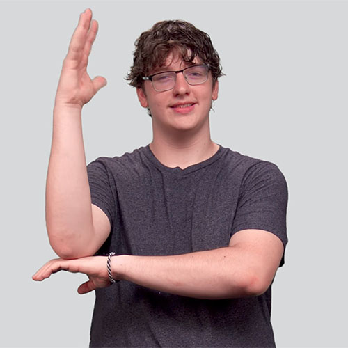 Person demonstrating the American Sign Language sign for 'tree' with one arm bent at the elbow and the hand pointing upwards, while the other arm is horizontal and supports the bent elbow.