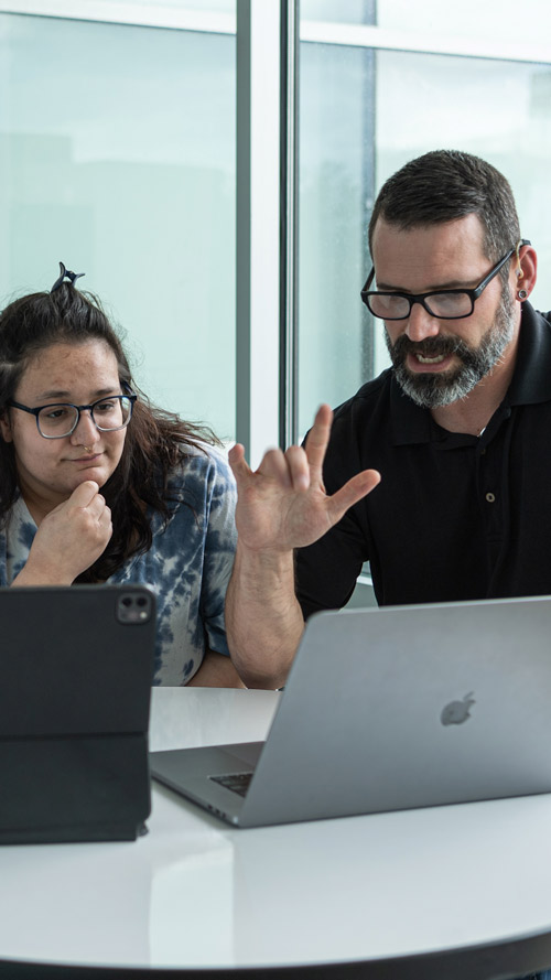 ernie showing something to student on laptop and signing