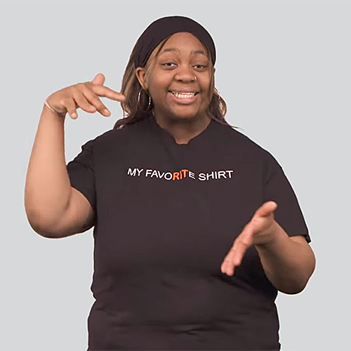 The image shows a person wearing a black t-shirt with the text "MY FAVORITE SHIRT" written on it. The person is making the sign for study. The background is plain gray.