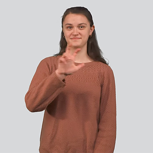 The image features a young woman with long dark hair tied back, wearing a brown textured sweater. She is smiling and using sign language. The background is a plain, light gray color.