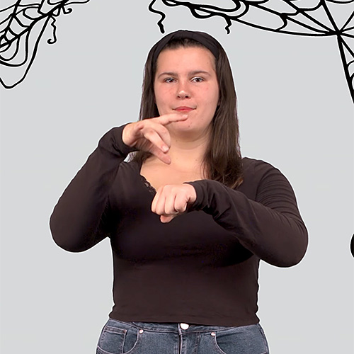 Person wearing a long-sleeve black top and jeans demonstrating a hand sign against a light gray background with black spiderweb illustrations in the corners.