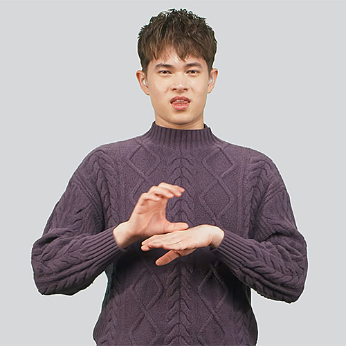 The image shows a person wearing a purple cable-knit sweater, standing against a light gray background. The individual is making the sign for 'chocolate.'