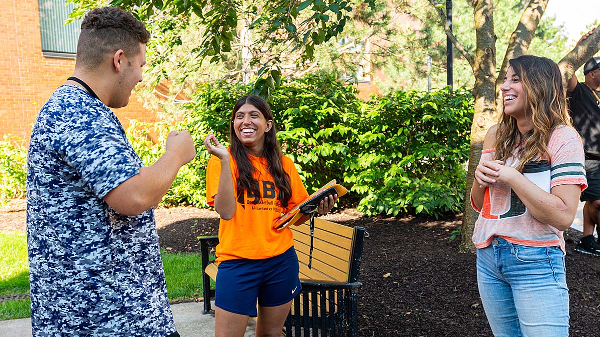 Three students having a conversation while standing outside.