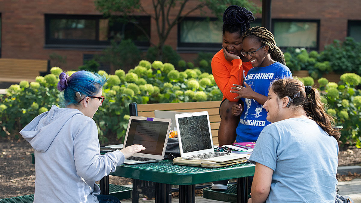 Four students using laptops on an outdoor picnic table