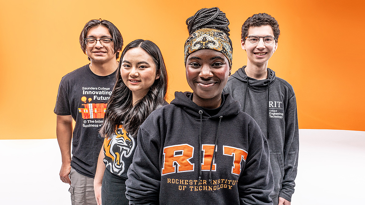 Four students stand facing the camera against a bright orange gradient background