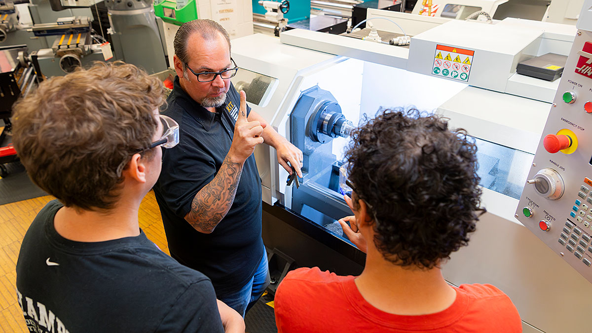 Three people in a workshop, with one person explaining the operation of a CNC machine to two others.