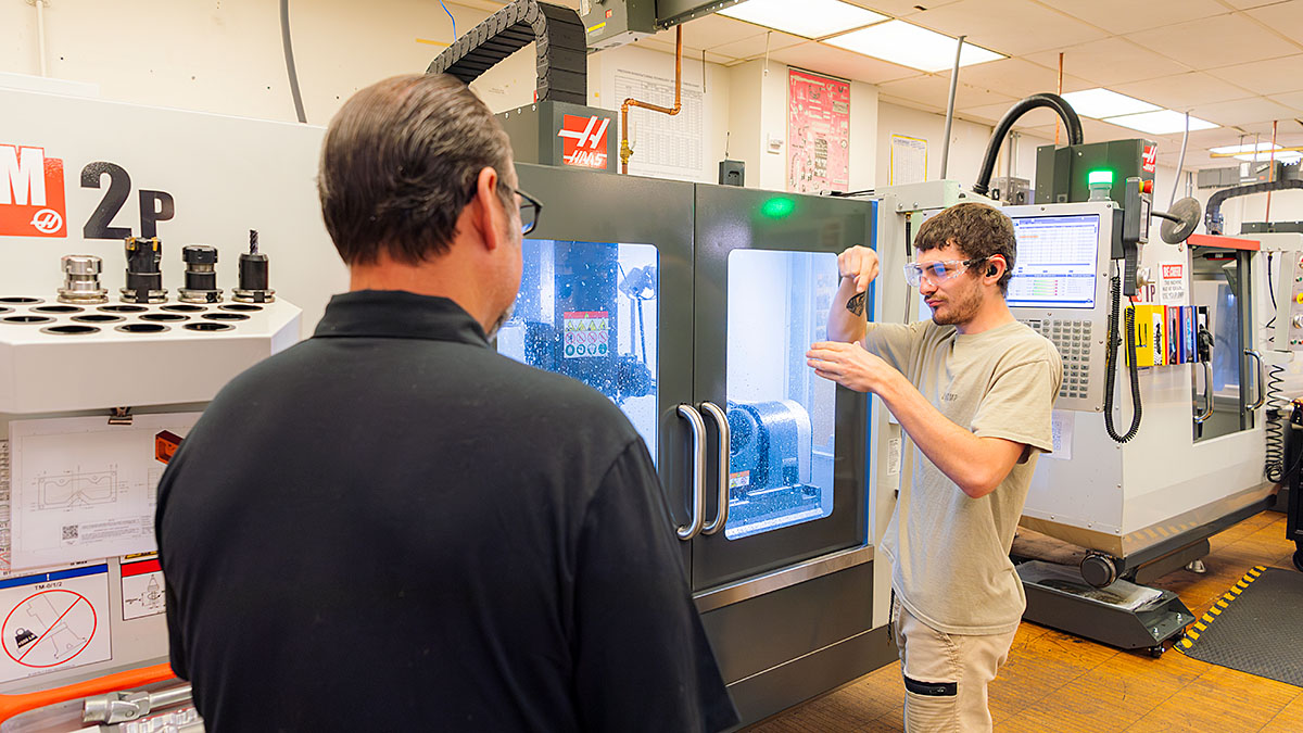 Two people discussing in front of CNC machine in workshop.