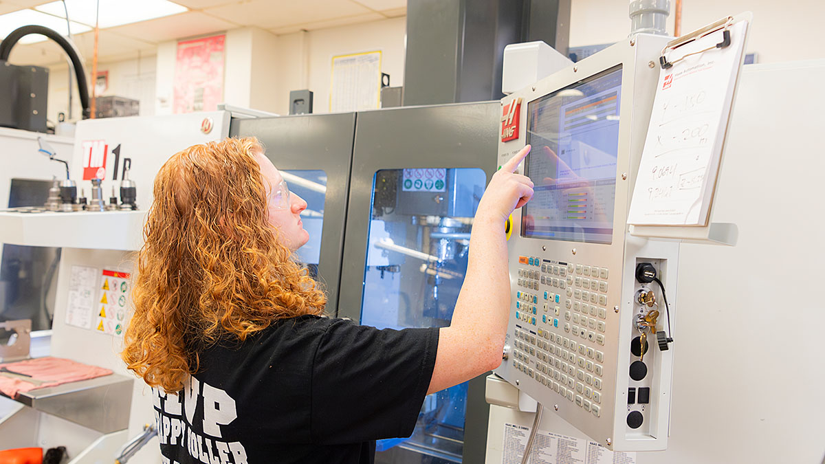 Person operating CNC machine control panel in workshop.