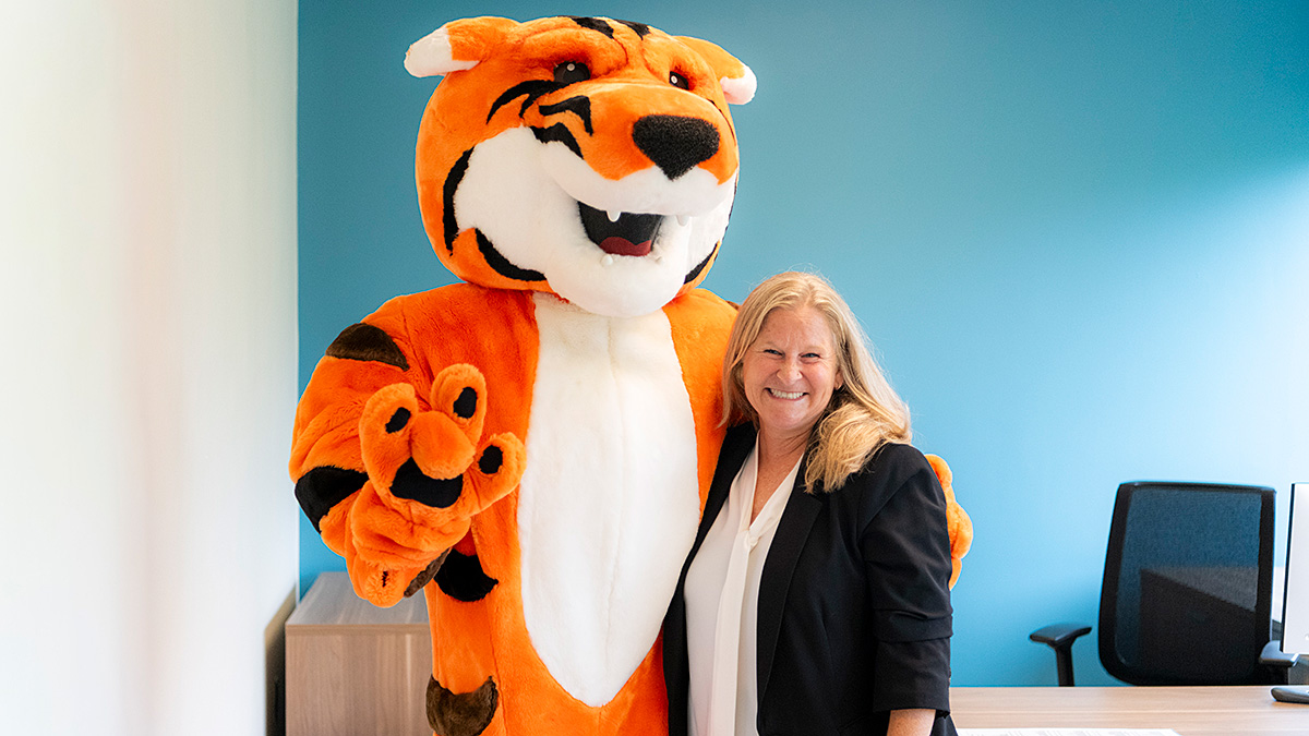 Flavia smiling and posing with the RIT tiger mascot inside an office.
