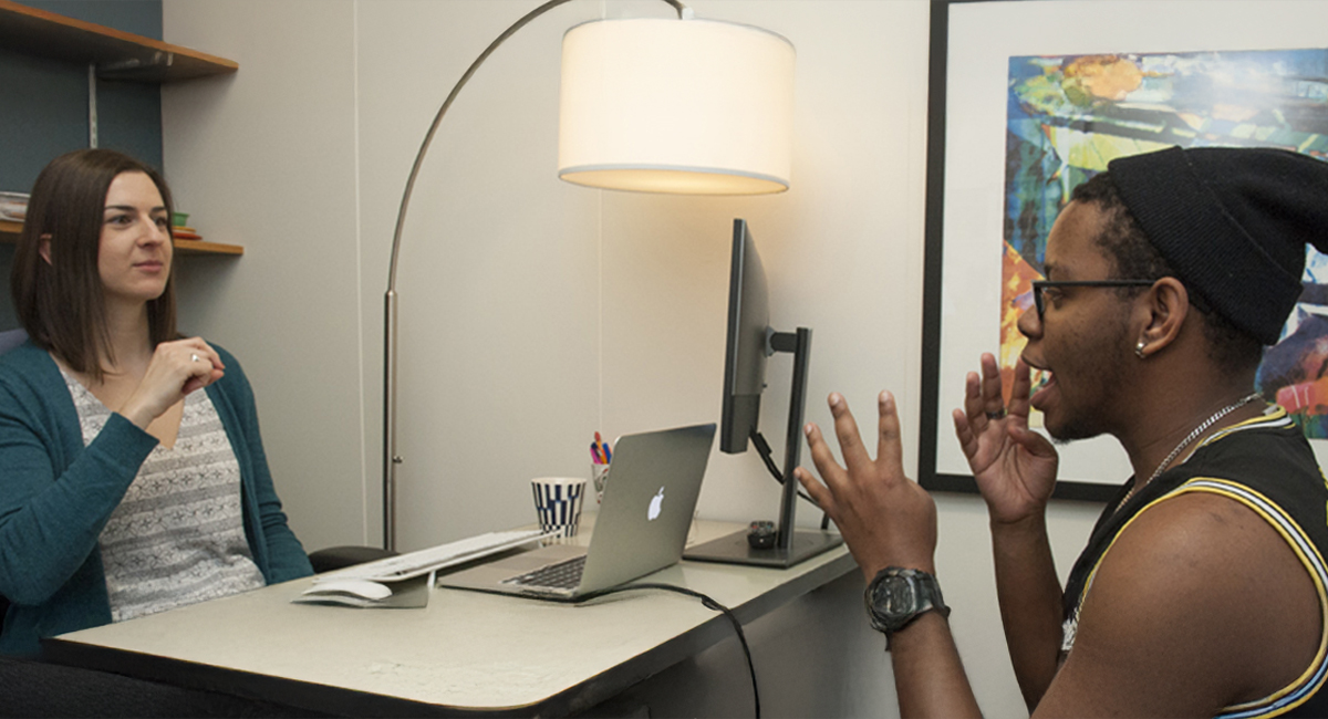 Counselor behind desk on left signing with student sitting at right