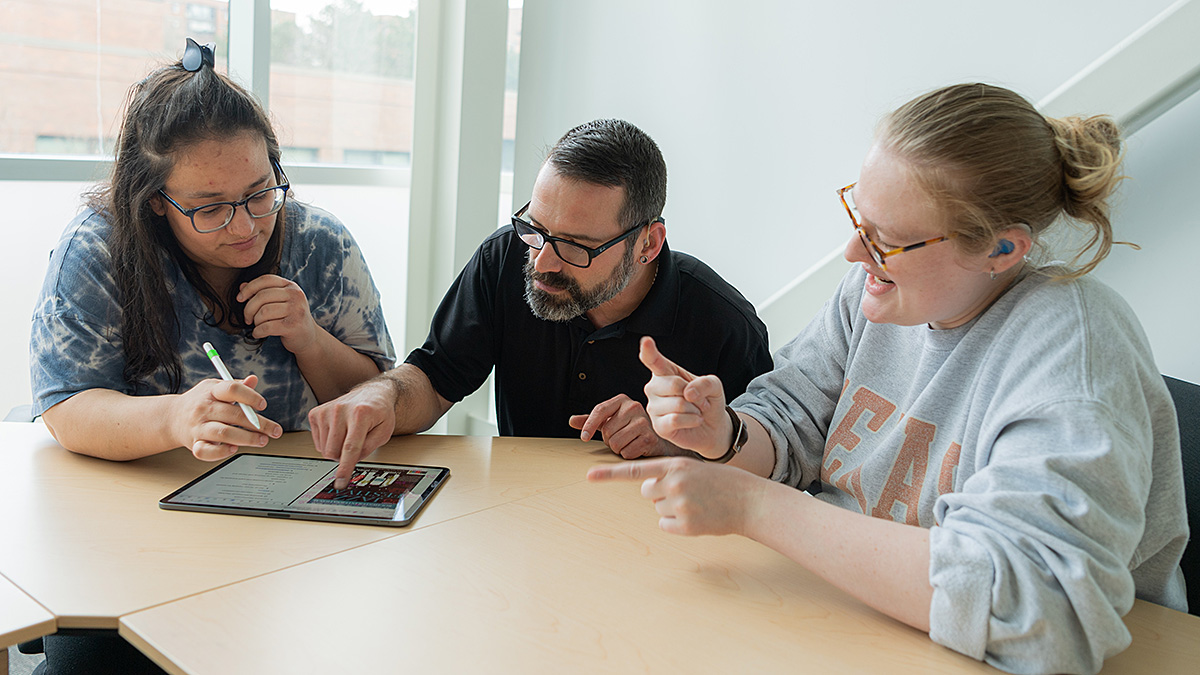 Professor tutoring two students using a tablet