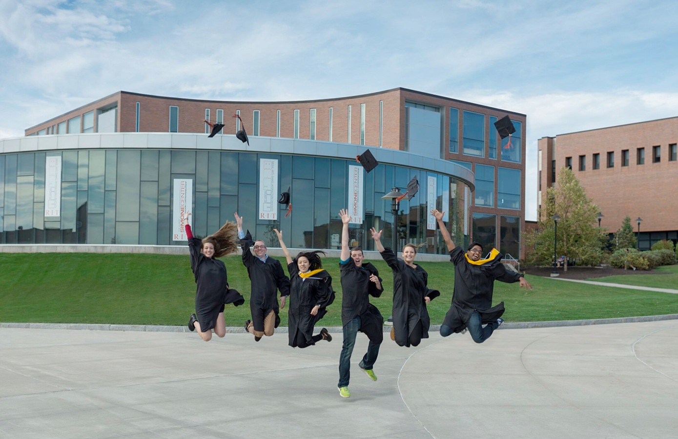 Students in caps and gowns jumping in air on campus