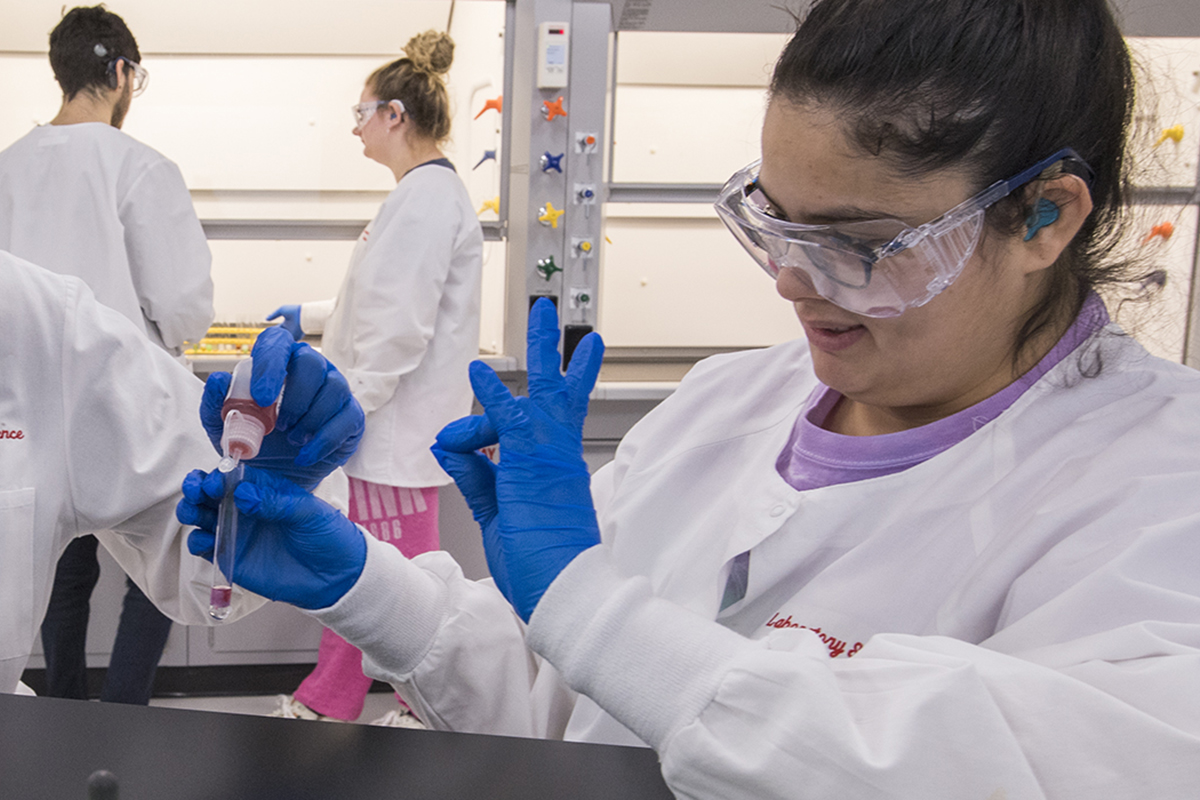 Students in lab coats and gloves filling test tubes