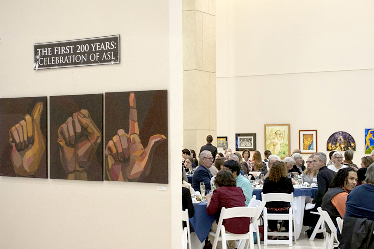 Photo of ASL artwork and people seated at tables