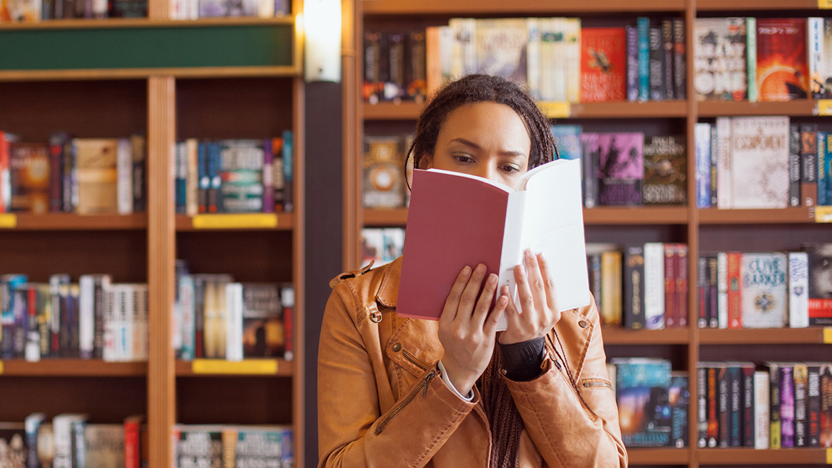 Girl reading book in front of shelves of books