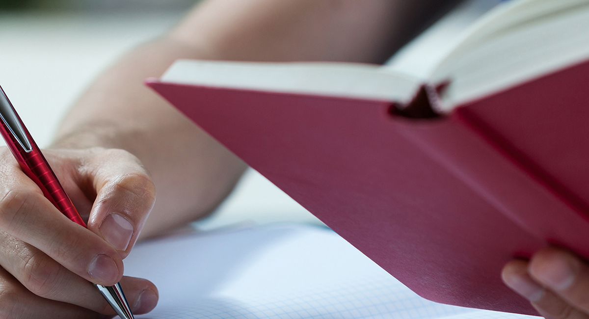 Student reading book and holding pen