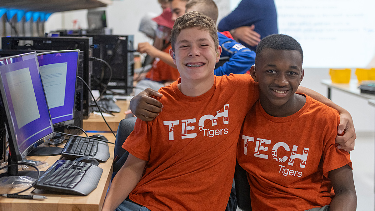 Two students wearing 'Tech Tigers' t-shirts, smiling with their arms around each other's shoulders