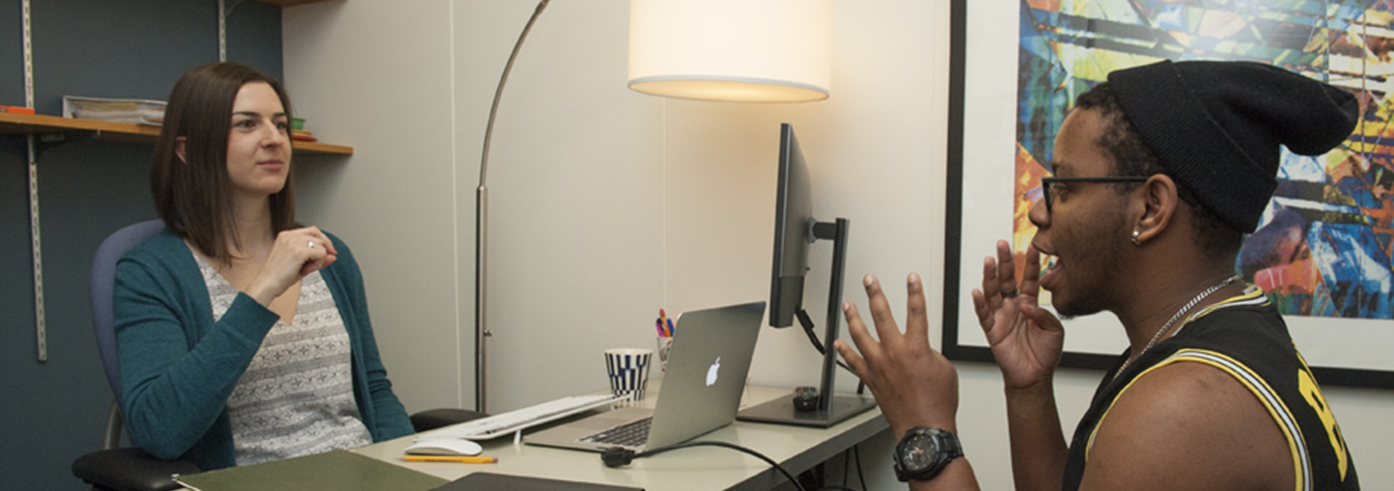 Counselor behind desk on left signing with student sitting at right