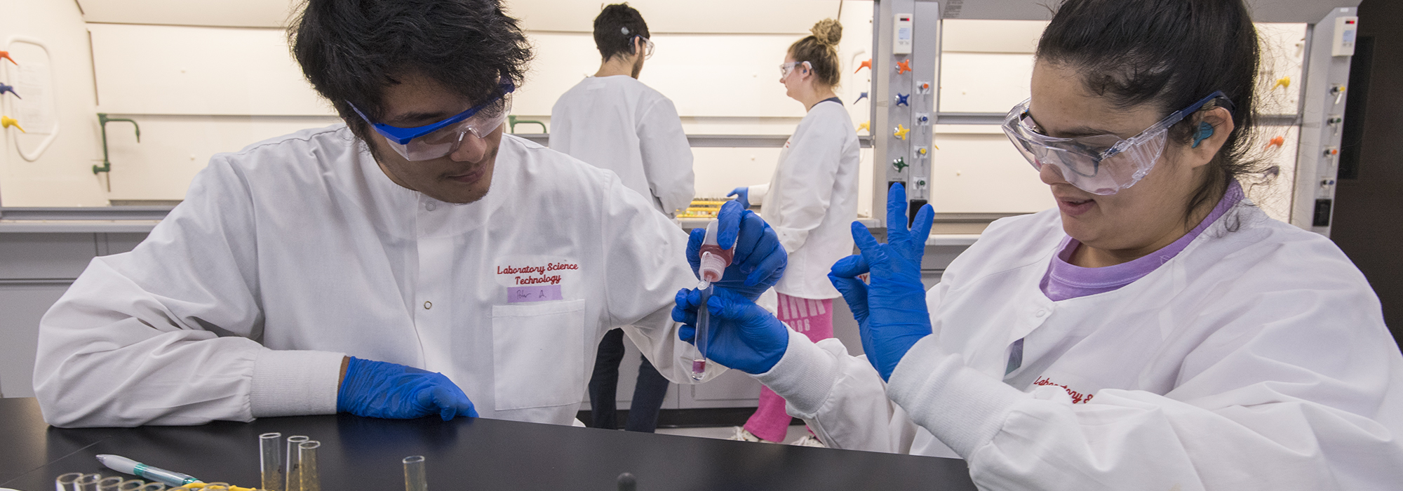 Students in lab coats and gloves filling test tubes