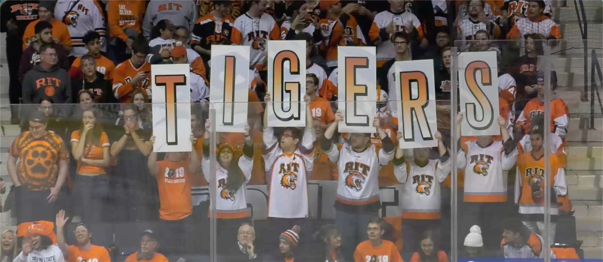 Students at RIT hockey game holding up letters that spell TIGERS