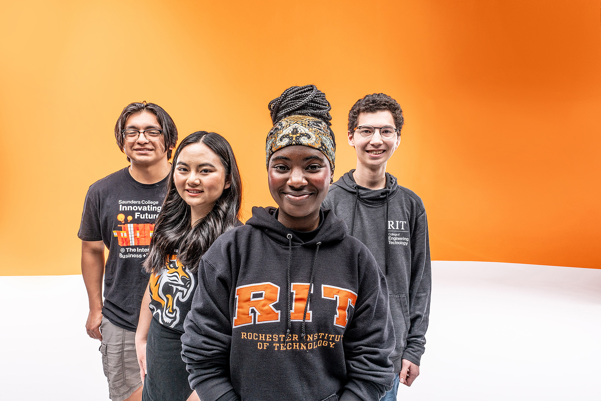 Four students stand facing the camera against a bright orange gradient background
