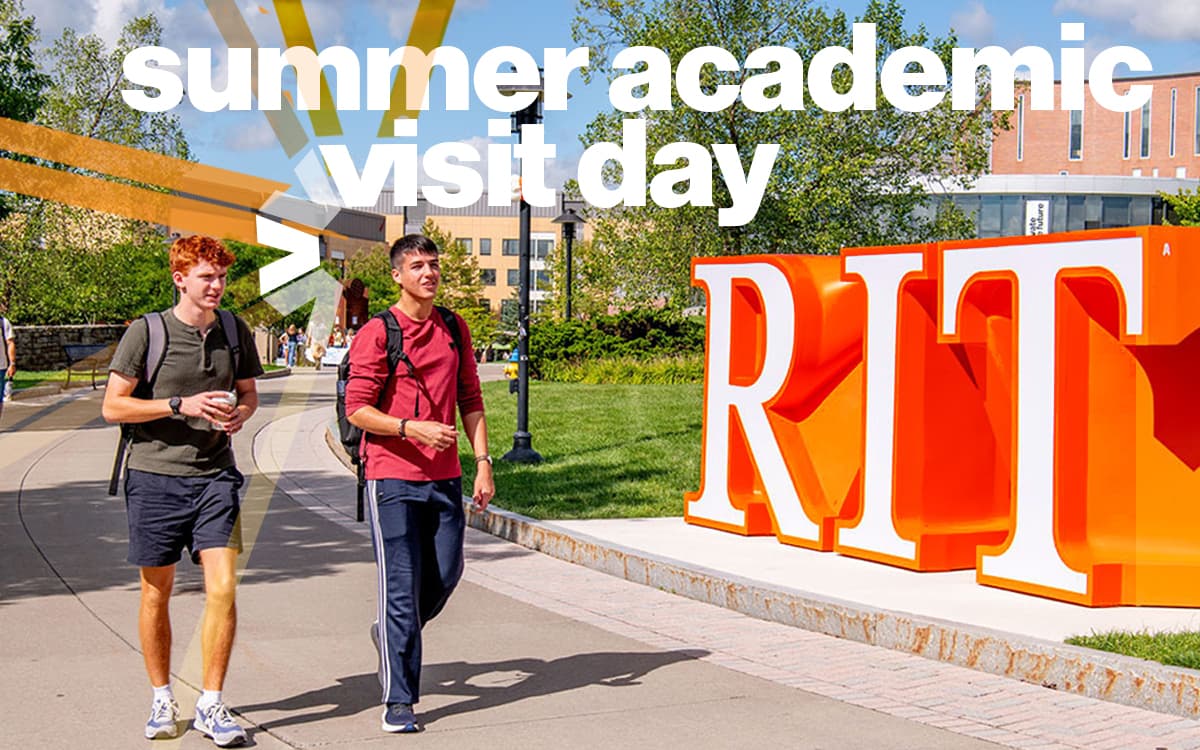 Two students walking by orange R I T sign.