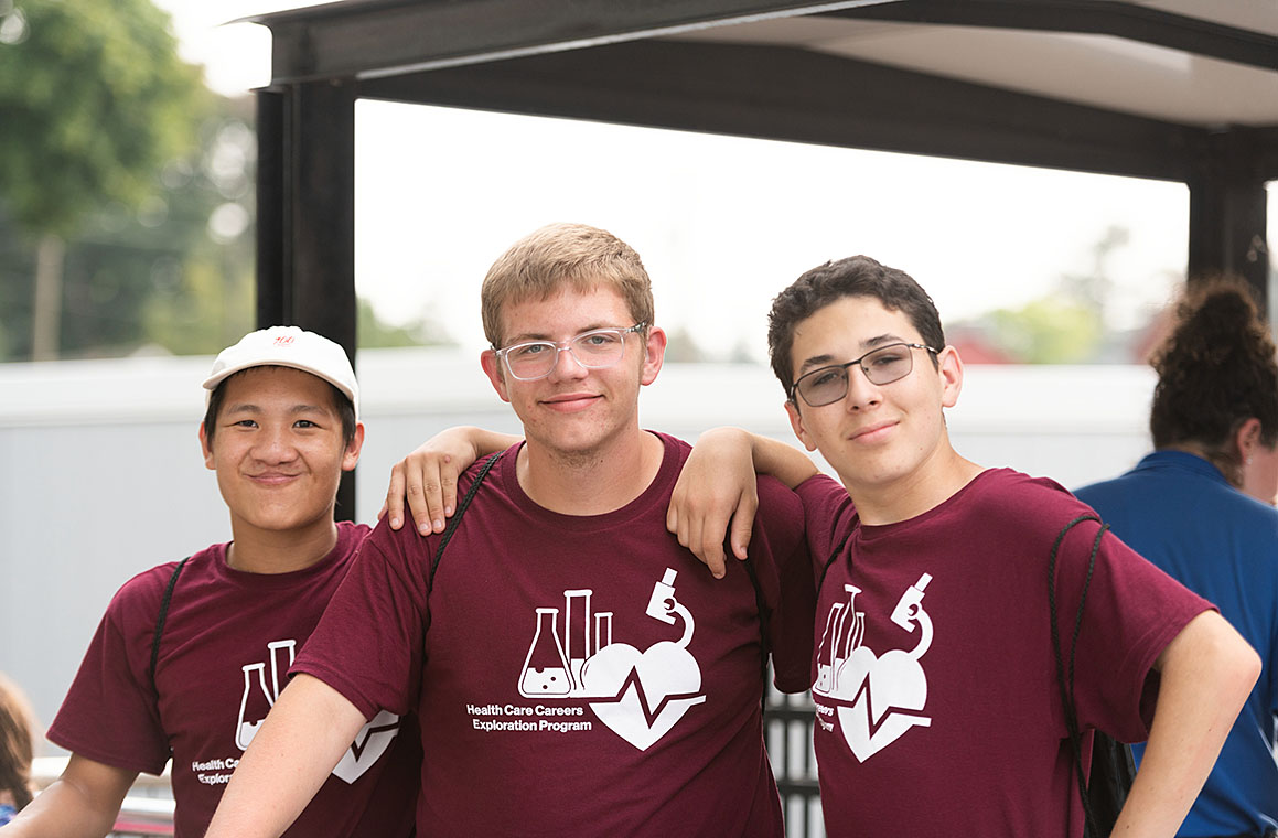 Three individuals wearing maroon t-shirts with a 'Health Care Careers Exploration Program' logo.
