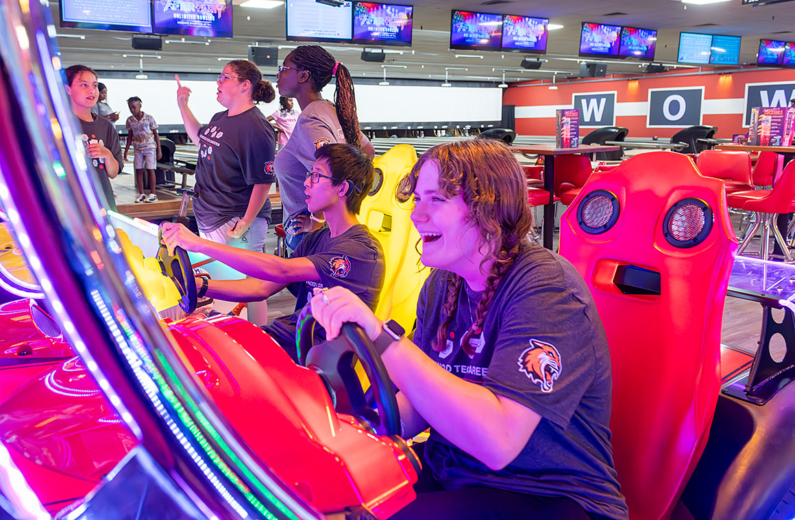 A group of people enjoying an arcade game in a brightly lit entertainment center, with some playing and others watching nearby.