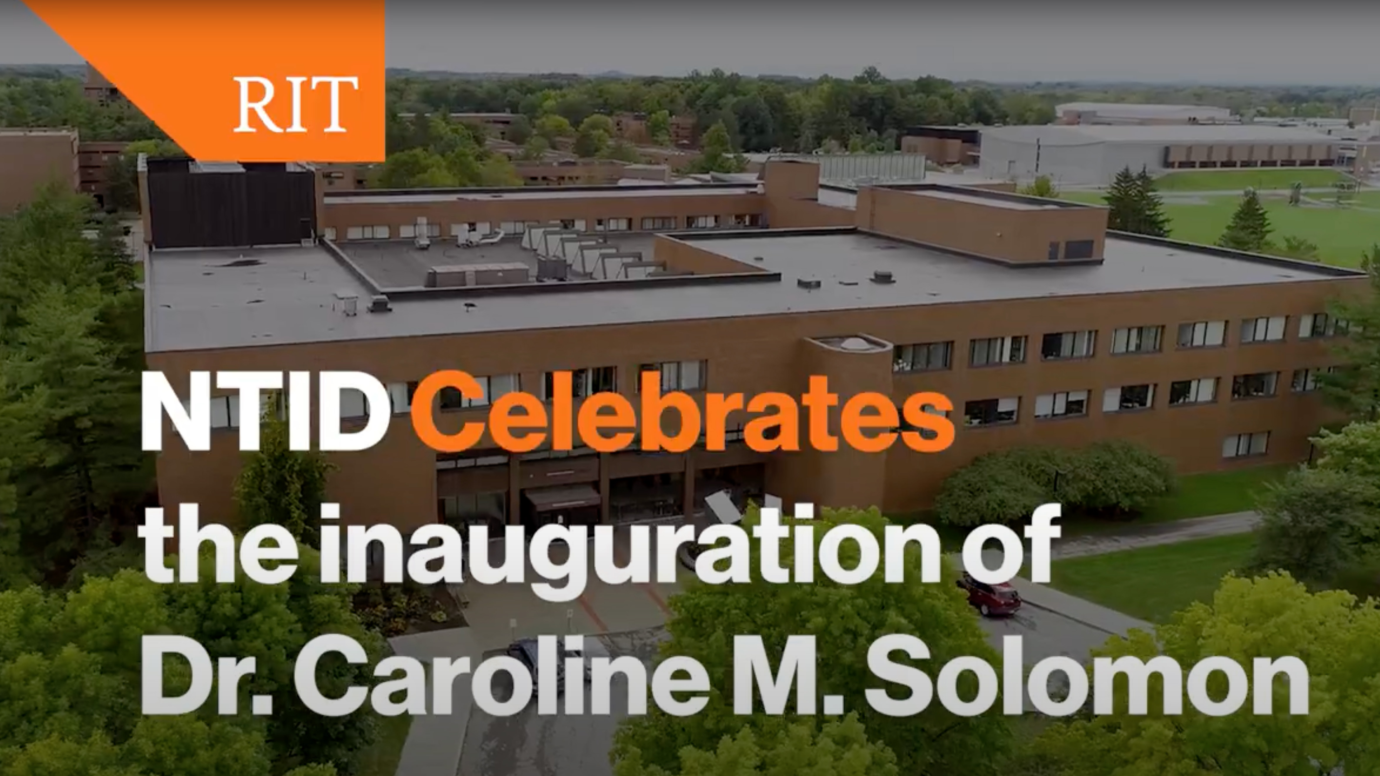 Aerial view of a large building on the RIT campus with text overlay: 'NTID Celebrates the inauguration of Dr. Caroline M. Solomon.'